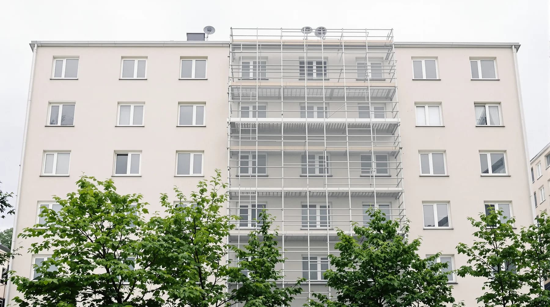 Flerbostadshus från sextiotalet med putsad fasad och ställning över en fasaddel