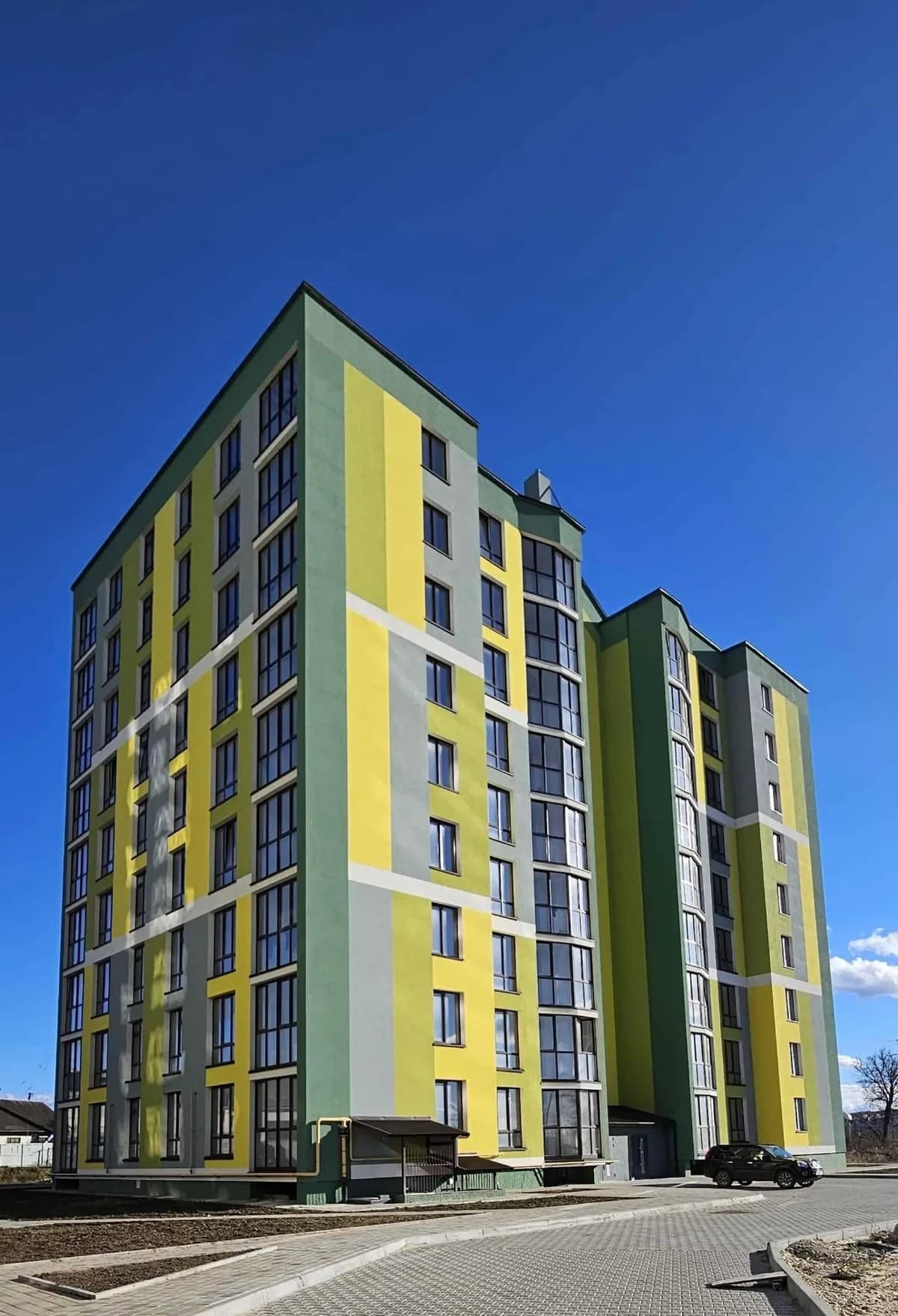 Nyproducerat flerbostadshus med putsad fasad i gult, grönt och grått mot klarblå himmel