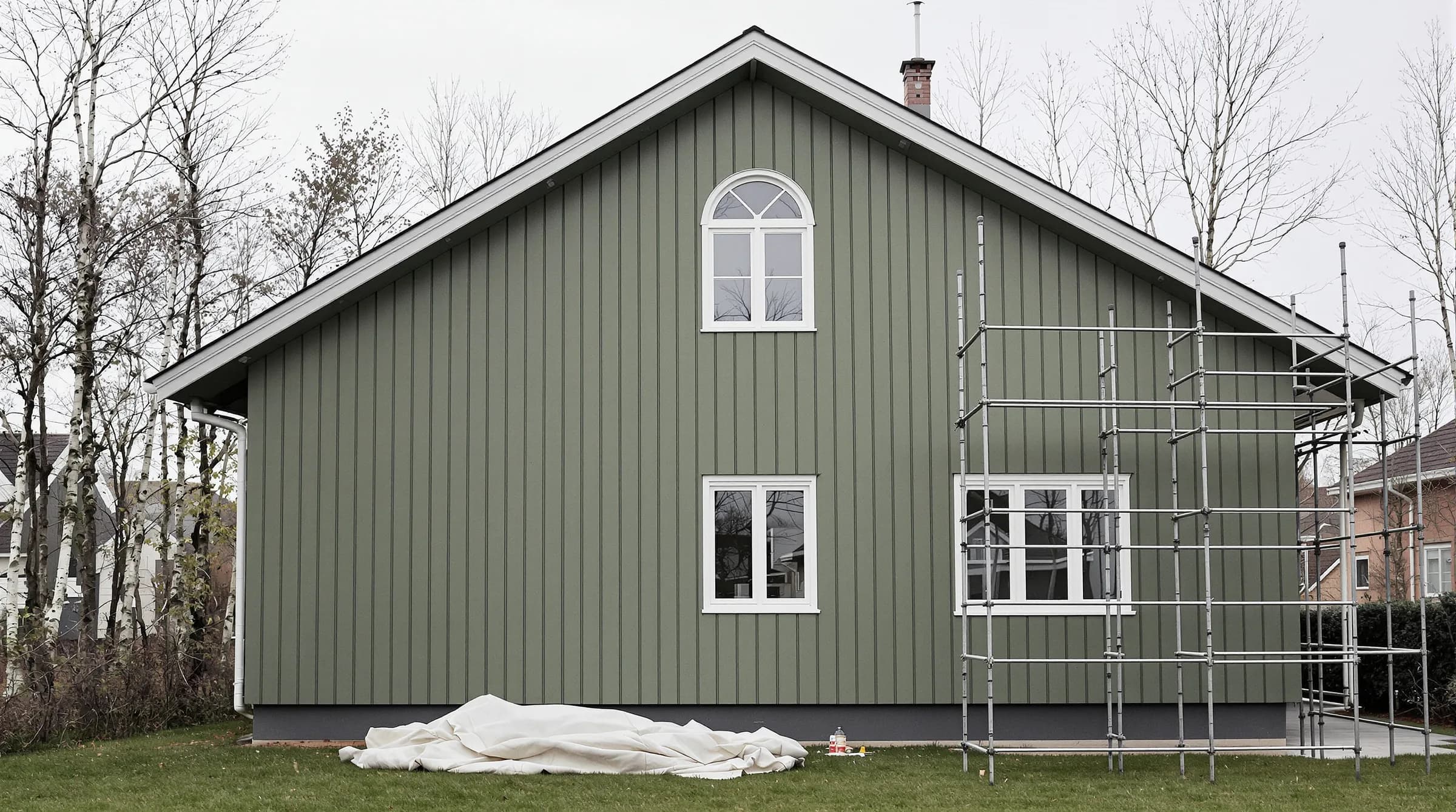 Svensk villa med stående träpanel under ommålning, byggnadsställning längs gaveln